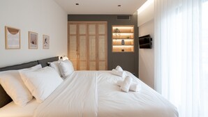 A modern hotel room with a neatly made bed, a wall-mounted TV, and a wooden wardrobe. - Acropolis Majestic view apartments (Athens)