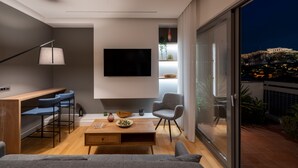 A modern living room with a flat-screen TV, a wooden coffee table, and a sofa. There are two bar stools and a chair. The room has a large window with a view of a cityscape. - Acropolis Majestic view apartments (Athens)
