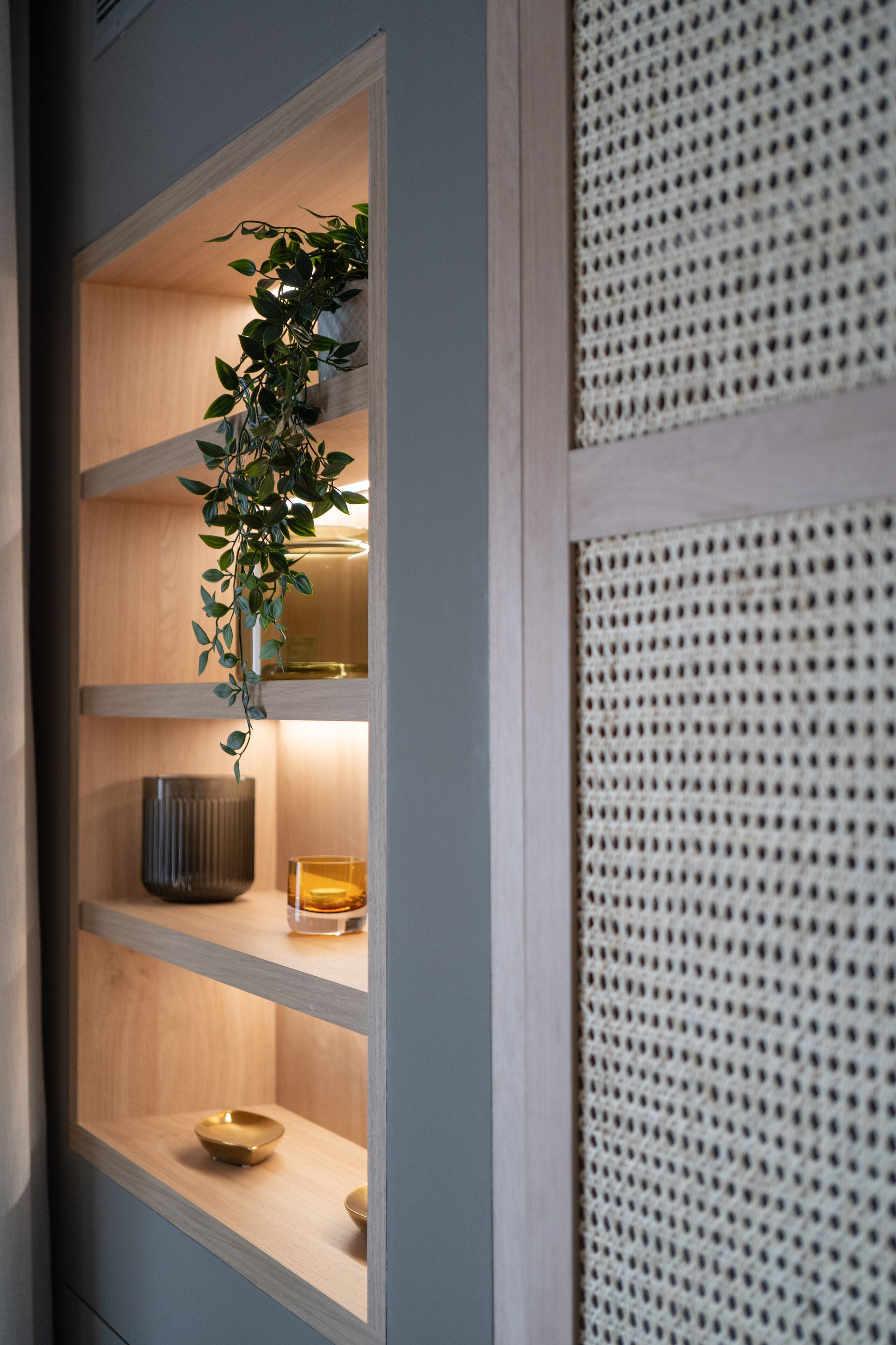 A wooden shelf unit with a potted plant, a candle, and a decorative bowl.