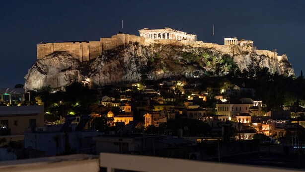 A night view of a historic building with a prominent cliff, illuminated by artificial lighting, overlooking a cityscape with various buildings. - Acropolis Majestic view apartments (Athens)