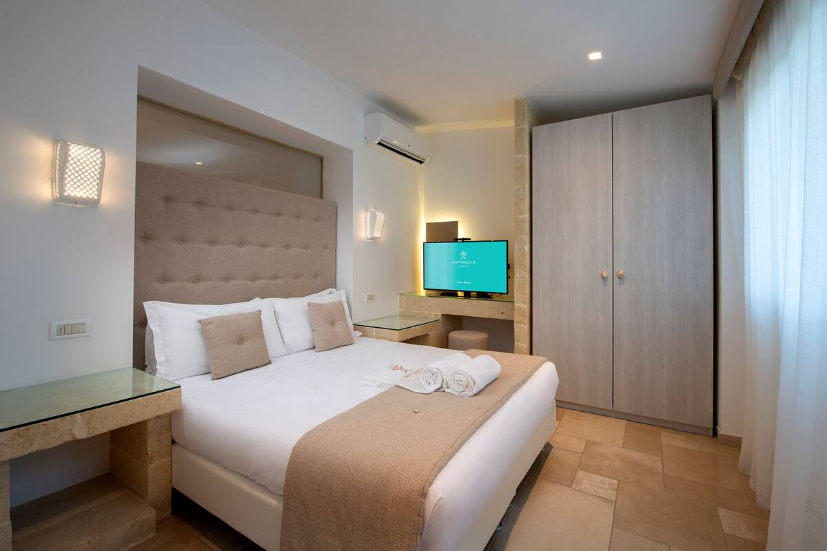 Ett hotellrum med en säng, ett skrivbord i glas, en tv och en garderob.