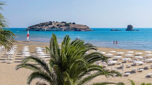 A beach with white umbrellas and lounge chairs, a sailboat, and rocky islands in the background. - Gattarella Family Resort - Standard Half-Board à buffet (Vieste)