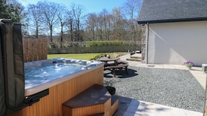 A hot tub with wooden steps and a table, surrounded by gravel and a wooden deck. - Woodend Croft (Ellon)