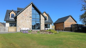 A modern house with a stone facade, large glass windows, and a well-maintained lawn. - Woodend Croft (Ellon)
