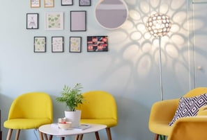 A room with two yellow chairs, a small round table with a bowl and a plant, and a floor lamp casting patterned shadows on the wall.