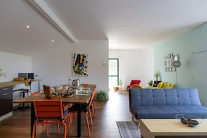 A modern living space with a dining area, a sofa, and a kitchen.
