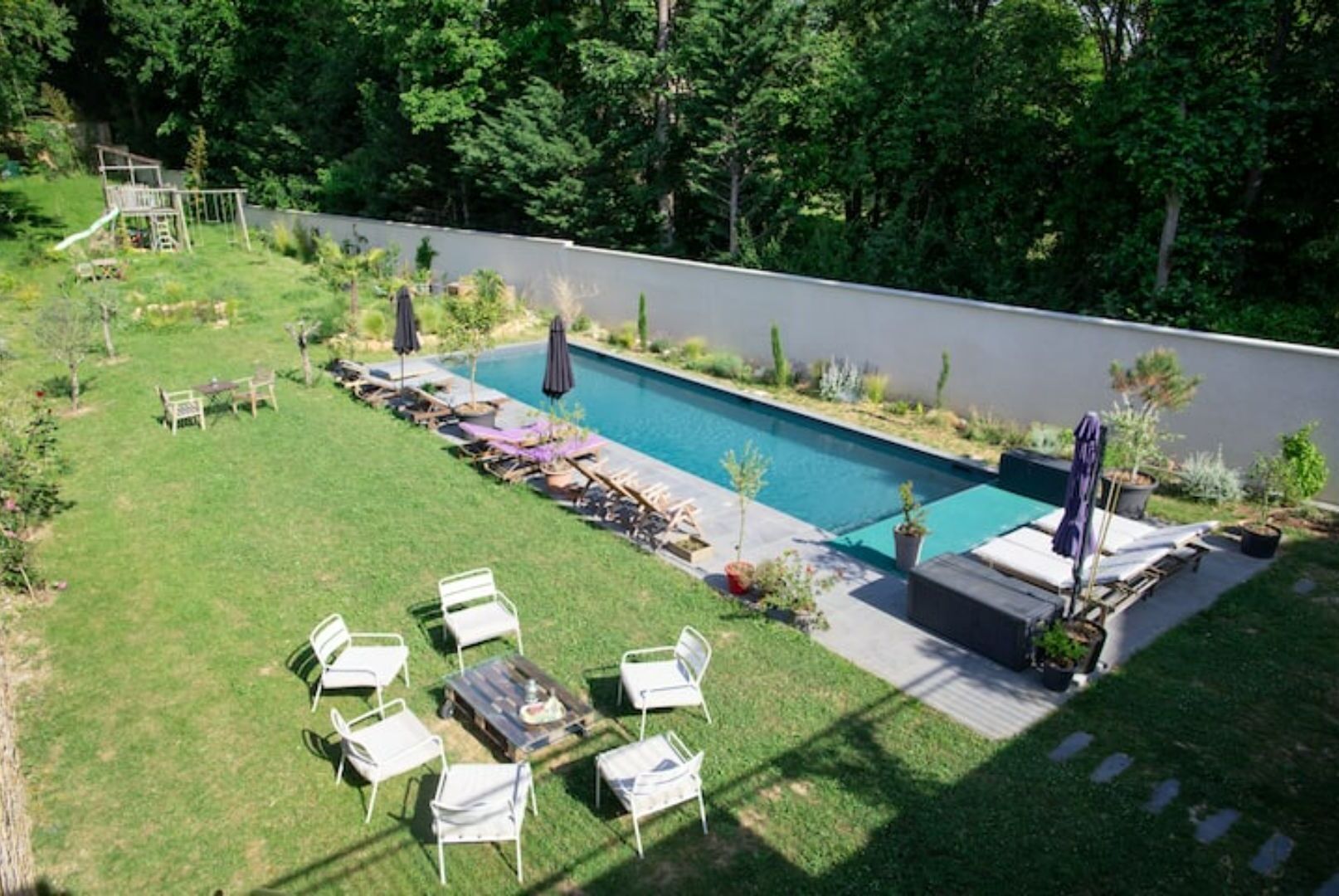 A backyard with a swimming pool, lounge chairs, and a small deck area.