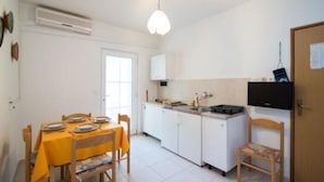 A compact kitchen with white cabinets, a dining table with yellow tablecloth, and a television mounted on the wall. - Apartments Boguvila - Two-bedroom Family Apartment With Terrace - (Supetar)