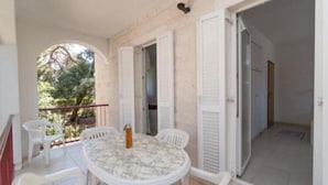 A balcony with a round table and chairs, a view of trees, and a door leading to another room. - Apartments Boguvila - Two-bedroom Family Apartment With Terrace - (Supetar)