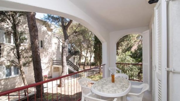 A balcony with a round table and chairs, overlooking a courtyard with trees and a building. - Apartments Boguvila - Two-bedroom Family Apartment With Terrace - (Supetar)