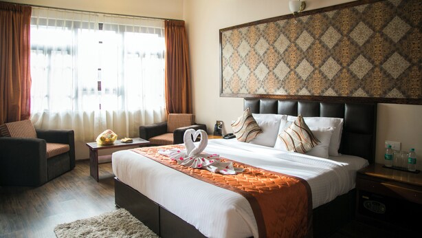 A hotel room with a large bed, a sofa, a small table, and a window with curtains. - New Orchid Lords Inn Gangtok  (Gangtok)