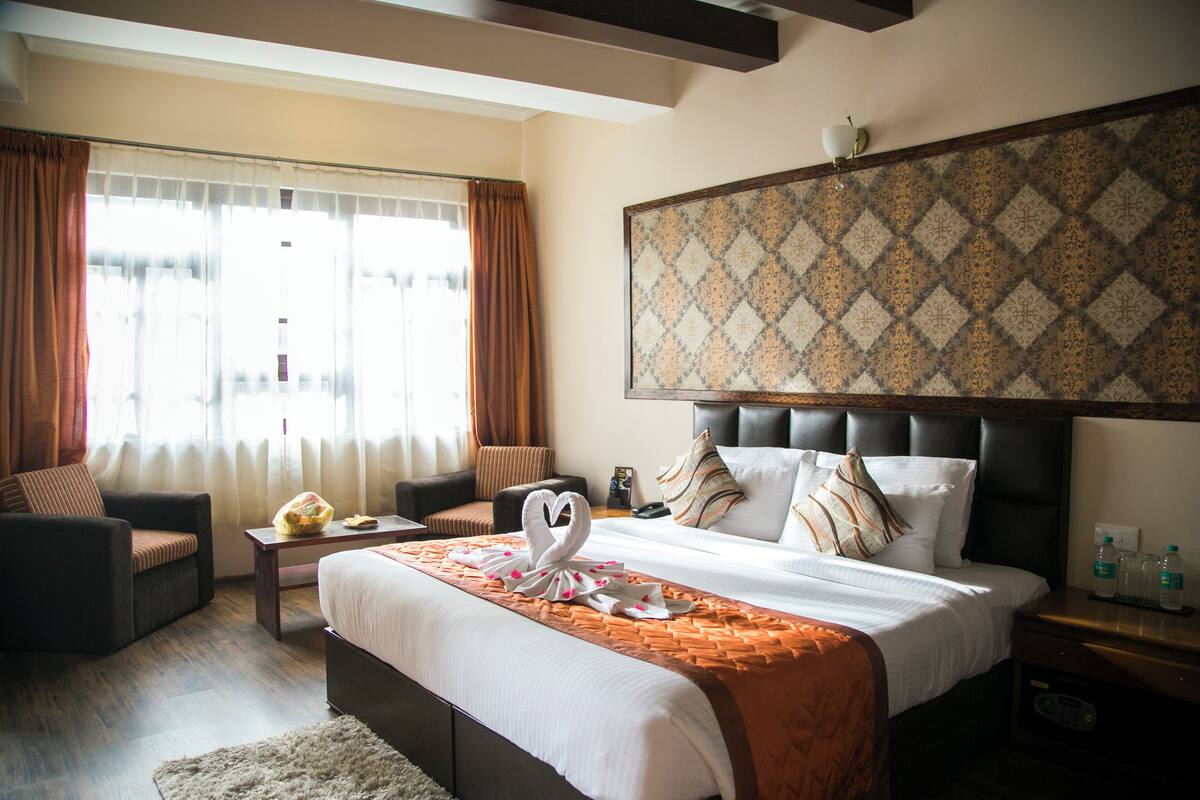 A hotel room with a large bed, a sofa, a small table, and a window with curtains.