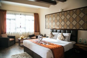 A hotel room with a large bed, a sofa, a small table, and a window with curtains. - New Orchid Lords Inn Gangtok  (Gangtok)
