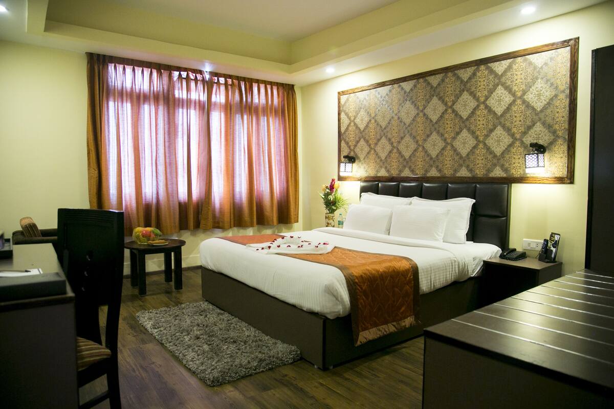 A hotel room with a bed, a desk, a chair, a nightstand, and a large window with curtains.
