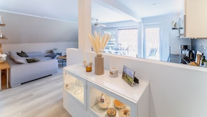 A modern living room with a sofa, a glass cabinet with decorative items, and a view of the kitchen through an open door. - Fewo am Schwanenteich mit Dachterrasse (Emden)