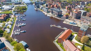 An aerial view of a river with boats docked along the banks, surrounded by buildings and greenery. - Fewo am Schwanenteich mit Dachterrasse (Emden)