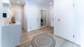 A modern hallway with white walls, a wooden floor, and a patterned rug. There are white doors and a mirror on the left. - Fewo am Schwanenteich mit Dachterrasse (Emden)