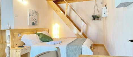 Un dormitorio con techo de madera, una cama con ropa de cama blanca y verde, una mesita de noche y una planta colgante.