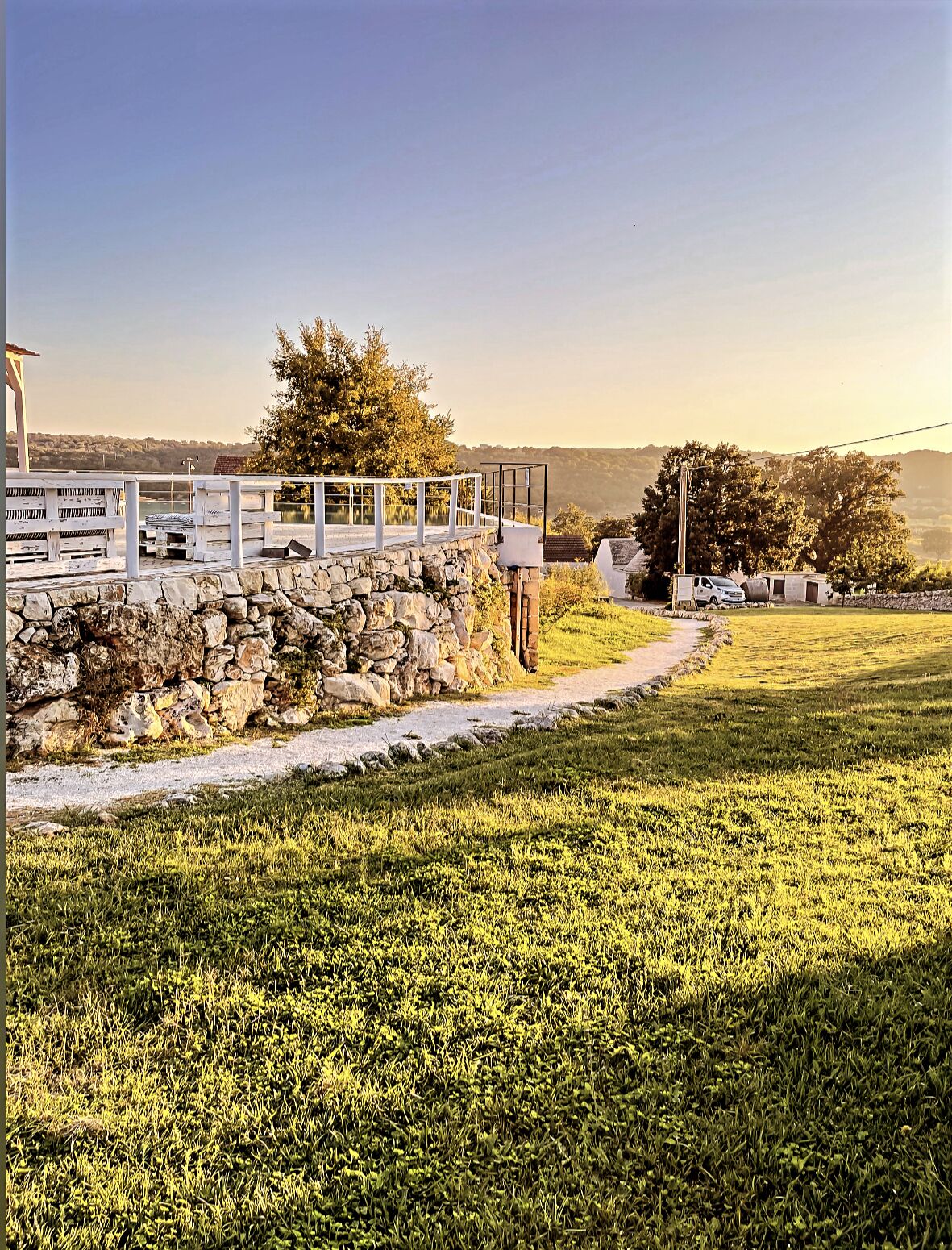 A stone wall with a white fence, a grassy area, and a view of a distant landscape.
