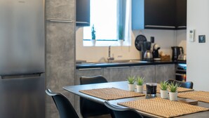 A modern kitchen with a stainless steel refrigerator, a dining table with woven placemats, and potted plants. - Duplex Penthouse with Sauna & Acropolis View (Athens)