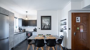 A modern kitchen with a dining area, featuring a large table, black chairs, and a wooden floor. - Duplex Penthouse with Sauna & Acropolis View (Athens)