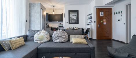 Una sala de estar moderna con un sofá gris, una mesa de centro y una cocina al fondo.