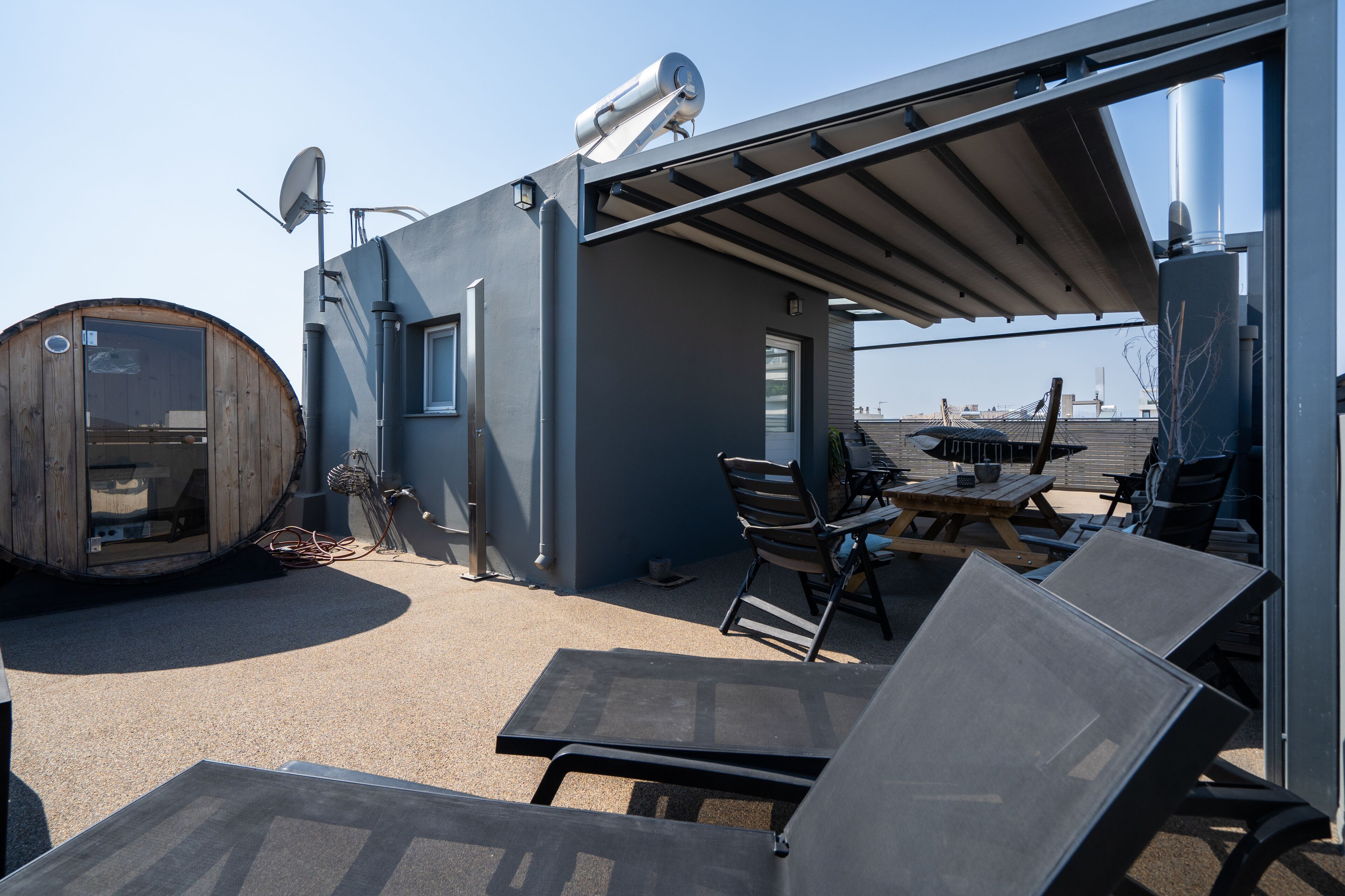 A rooftop terrace with a wooden barrel, metal chairs, and a table.