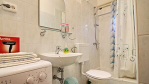 A bathroom with a sink, toilet, and shower. There is a mirror above the sink, and a glass shelf with toiletries. - Apartments Marita - Two Bedroom Apartment (Korčula)