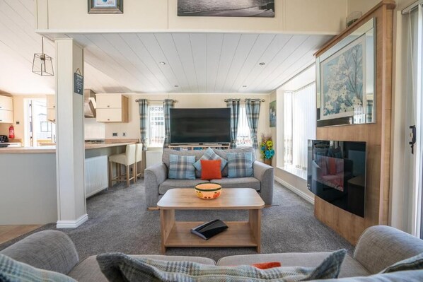 A cozy living room with a sofa, coffee table, and a television. There is a kitchen area with cabinets and a dining table.