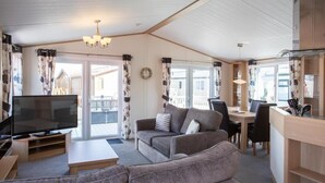 A modern living room with a flat-screen TV, a sofa, and a dining area with a table and chairs. - Barmouth Bay Holiday Park (Talybont)