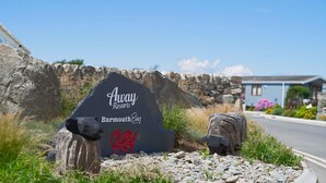 A sign for Away Resorts in Barmouth Bay with a stone wall and a stone animal figure. - Barmouth Bay Holiday Park (Talybont)