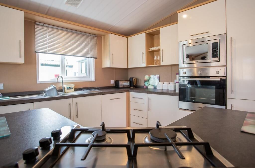 A modern kitchen with a gas stove, microwave, oven, and a window with blinds.
