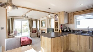A compact kitchen with wooden cabinets, a central island, and a dining area with a table and chairs. - Barmouth Bay Holiday Park (Talybont)