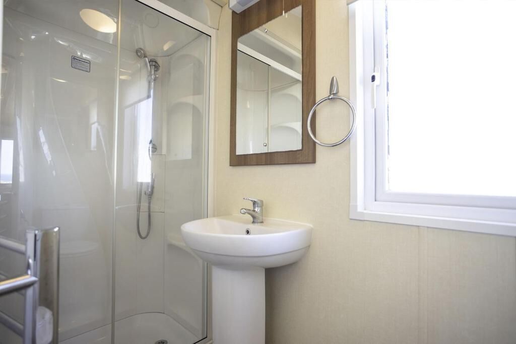 Une salle de bain avec une douche à parois de verre, un lavabo blanc et un miroir avec un cadre en bois.
