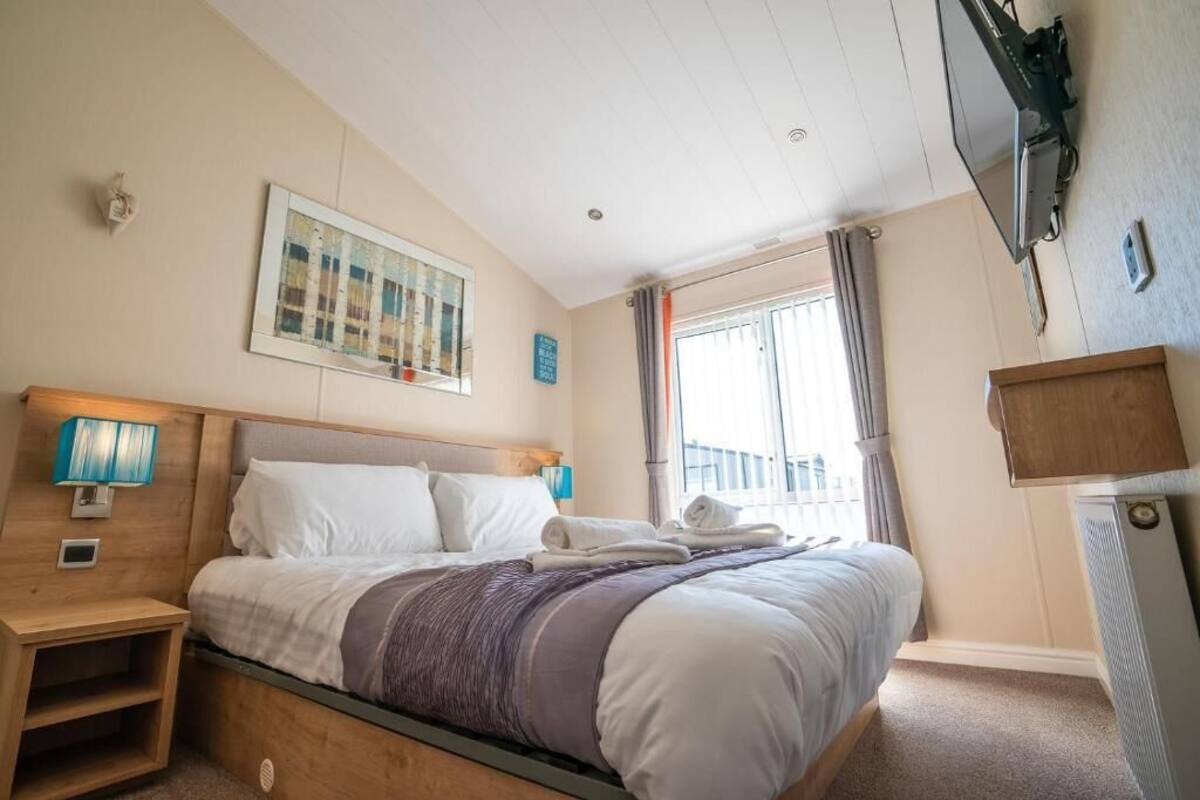 Une chambre d’hôtel avec un lit, des lampes de chevet, un tableau, une fenêtre avec des rideaux et un téléviseur fixé au mur.