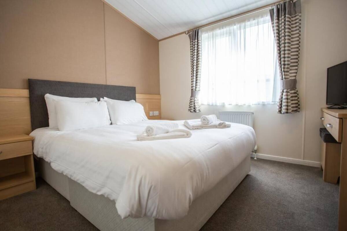 Une chambre d’hôtel avec un grand lit, une table de chevet en bois, une télévision et une fenêtre avec des rideaux.