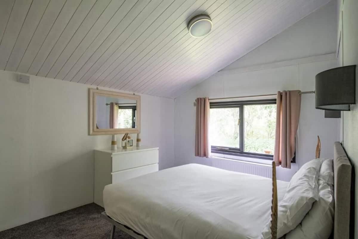 Une chambre à coucher avec un lit, une commode, une fenêtre avec des rideaux et un luminaire au plafond.