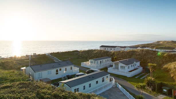 A coastal residential area with multiple houses, some with white railings, and a clear view of the sea. - Barmouth Bay Holiday Park (Talybont)