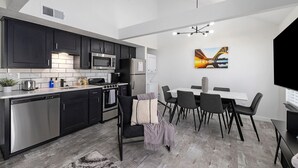 A modern kitchen with dark cabinets, stainless steel appliances, and a dining area with a white table and black chairs.