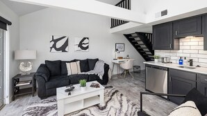 A modern apartment with a living room, dining area, and kitchen. There is a staircase connecting the two floors.
