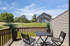 Une terrasse couverte avec une table et des chaises, une vue sur une maison et, au fond, une zone herbeuse.