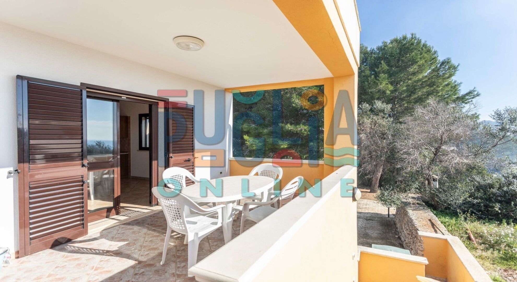 A balcony with a table and chairs, a sliding door, and a view of trees and hills.