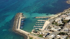 An aerial view of a coastal marina with multiple docks and boats, surrounded by residential buildings.
