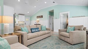 A living room with a beige sofa, teal pillows, and a patterned rug. There is a sign on the wall that reads "Welcome to the Beach."