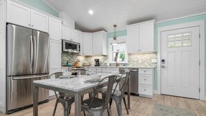 A modern kitchen with white cabinets, stainless steel appliances, and a marble countertop.