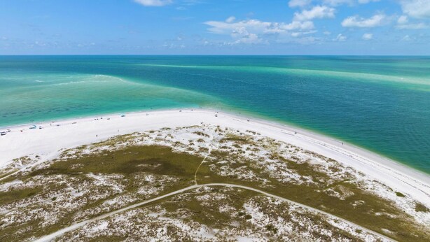 An aerial view of a beach with clear turquoise waters and a white sandy shore.