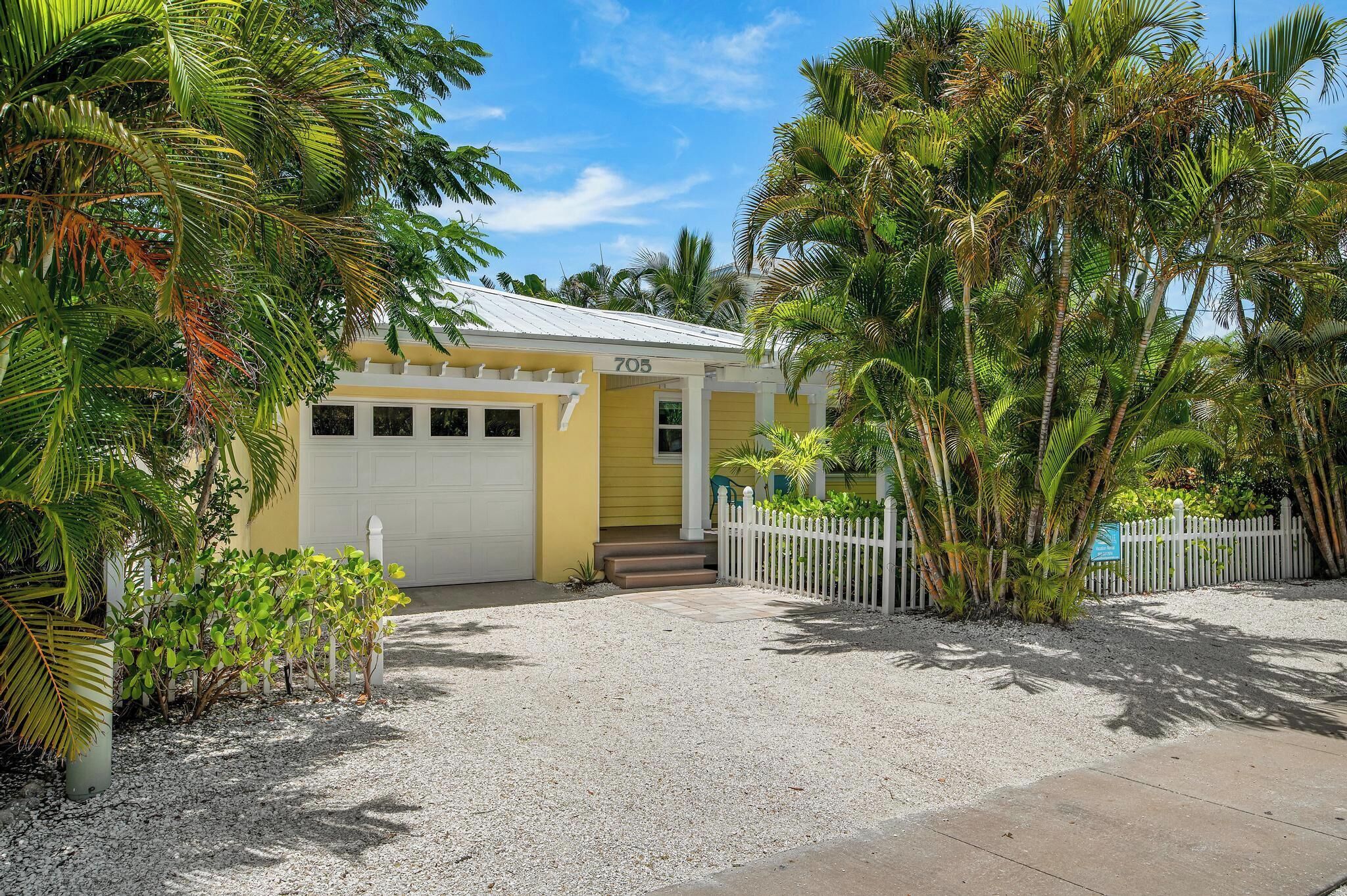 A yellow building with the number 705, surrounded by palm trees and a white fence.