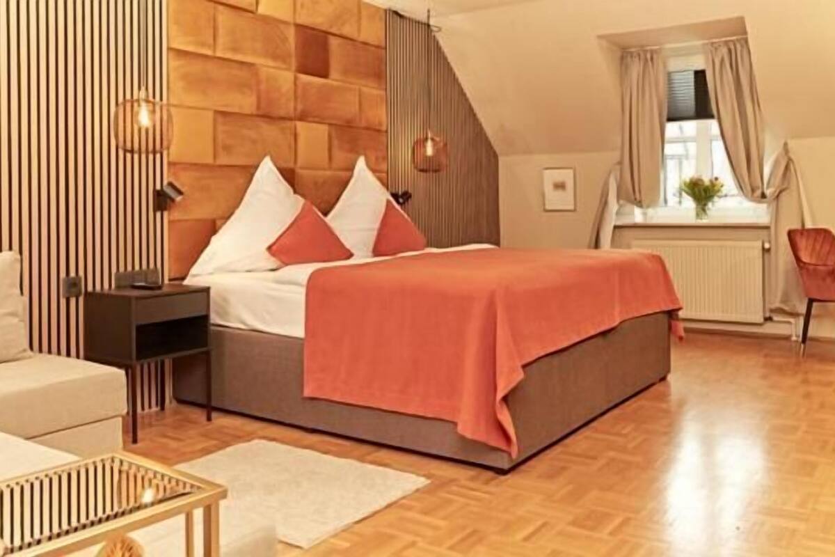 A modern bedroom with a wooden headboard, a bed with a red blanket, a nightstand, a desk, and a chair.