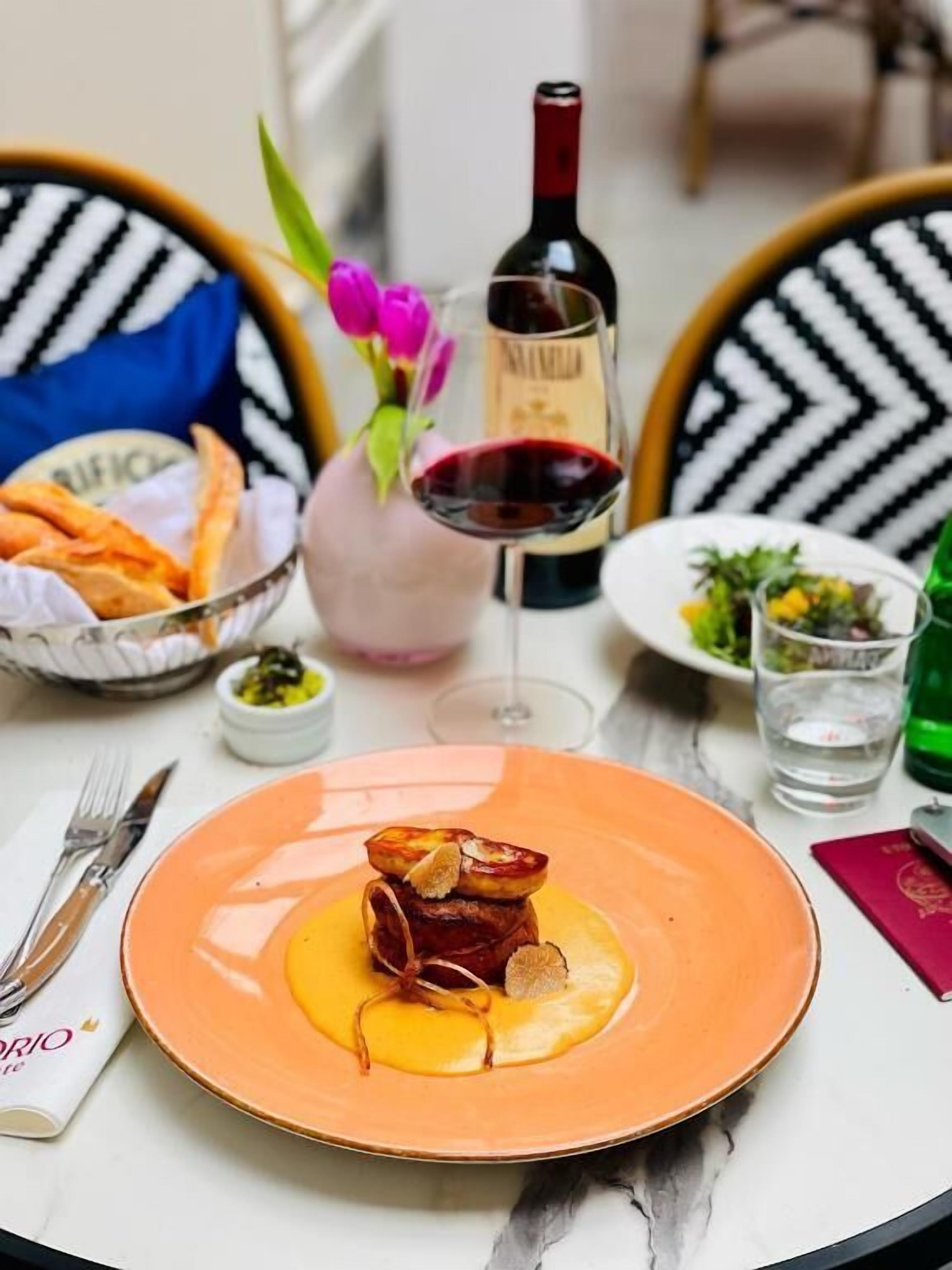 A dining table with a plate of food, a bottle of wine, and a vase with flowers.