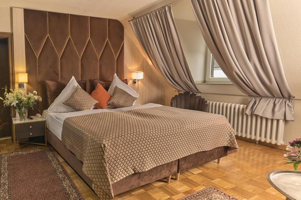Un dormitorio con una cama grande, una mesita de noche, una lámpara, un radiador y una ventana con cortinas.